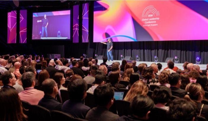 Speaker presenting on stage to a large conference audience
